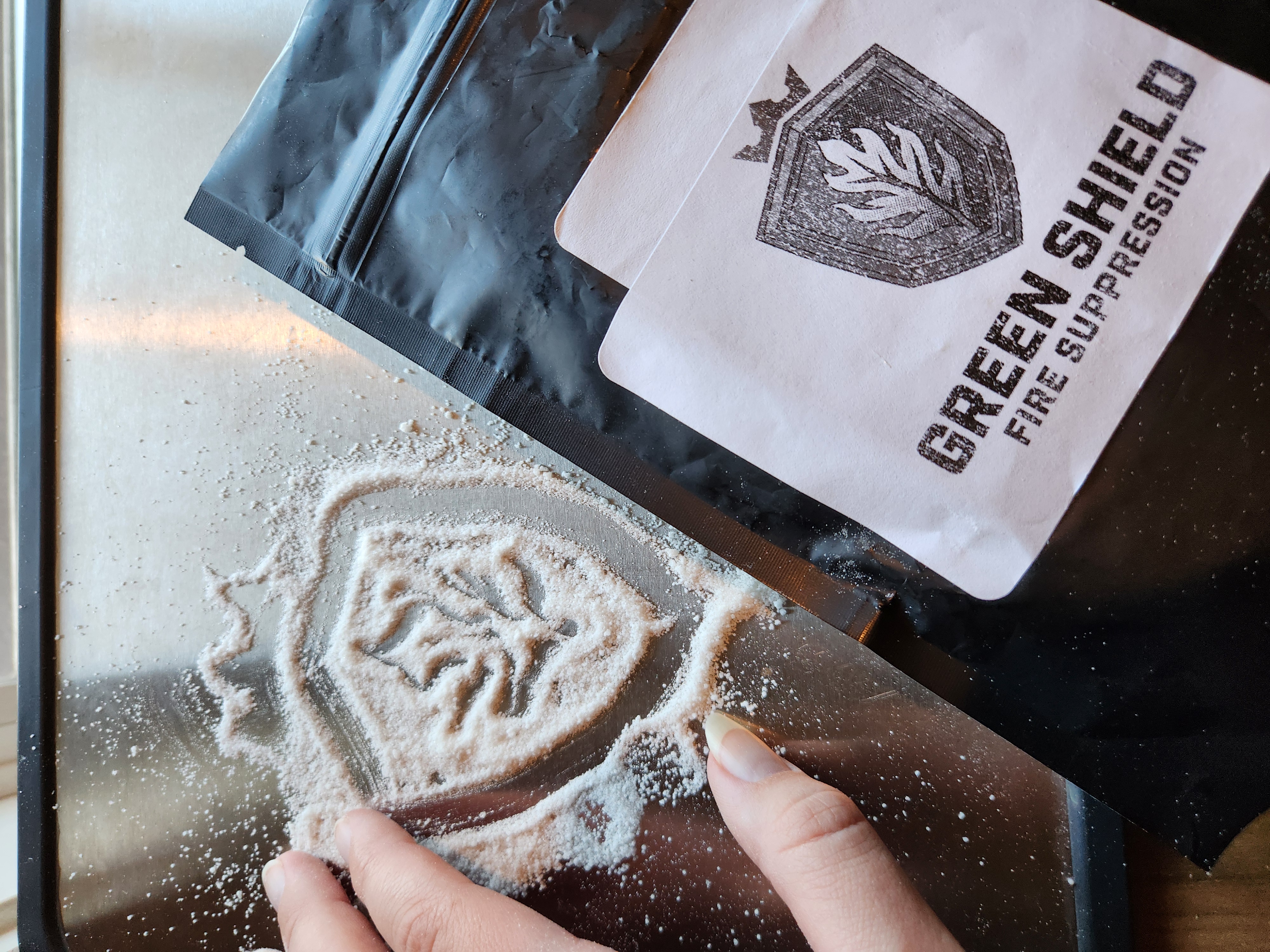 Green Shield Fire sample package with fingers touching the powdered hydrogel.